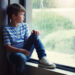 Child sitting by a window on a rainy day